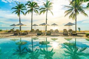 Hermosa sombrilla de lujo y una silla alrededor de la piscina al aire libre en el hotel y resort con palmera de coco en el cielo al atardecer o al amanecer foto