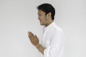 Young Asian man wearing white shirt gives greeting hands at with a big smile on her face. Indonesian man on gray background. Eid Mubarak photo