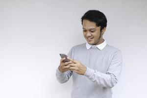 un joven asiático inteligente está feliz y sonriendo cuando usa un teléfono inteligente en el fondo del estudio foto
