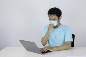 Young Asian man wear medical mask is cough when working with laptop on the table. photo