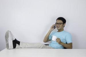 el joven asiático se siente feliz y sonríe cuando habla por teléfono con la pierna sobre la mesa. foto