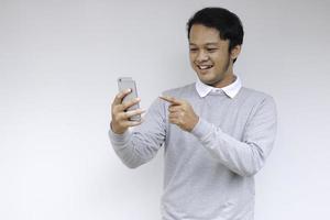 Young Asian man shocked and happy with what he see in the smartphone on isolated grey background. photo