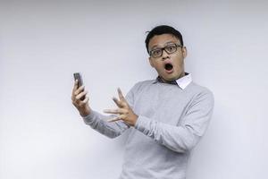 Wow face of Your Asian man shocked what he see in the smartphone on isolated grey background. photo