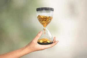 reloj de arena con monedas de oro en la mano, el tiempo es concepto de dinero foto