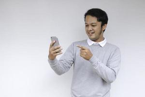 Young Asian man shocked and happy with what he see in the smartphone on isolated grey background. photo