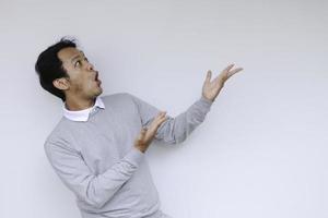 Young asian man waer white shirt is surprised and shouting wow with pointing right with his finger isolated on gray background with copy space fot your text. photo