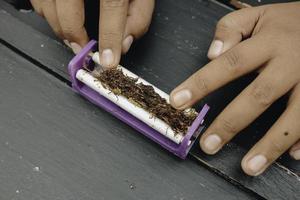 la mano del hombre hace un cigarrillo con herramientas tradicionales rodantes, primer plano de las manos. foto