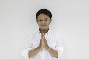 Young Asian man wearing white shirt gives greeting hands at with a big smile on her face. Indonesian man on gray background. Eid Mubarak photo