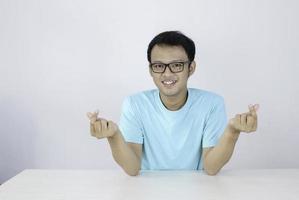 Young Asian Man showing love Korean sign with isolated white background. Indonesian man wearing blue shirt. photo