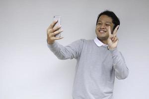 Young Asian Man is happy and smile when making a video call and take selfie, against white background photo