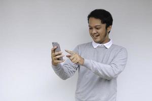 joven asiático conmocionado y feliz con lo que ve en el teléfono inteligente en un fondo gris aislado. foto