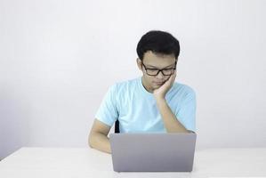 Young Asian Man is serious and focus when working on a laptop and document on the table. Indonesian man wearing blue shirt. photo