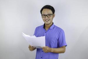 el joven asiático sonríe y es feliz cuando mira un documento en papel. hombre indonesio con camisa azul. foto