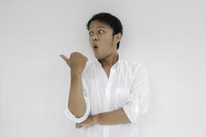 Young asian man war white shirt is surprised and shouting wow with pointing right with his finger isolated on gray background photo