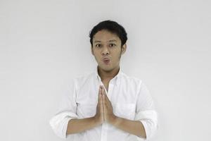 Young Asian man wearing white shirt gives greeting hands at with a big smile on her face. Indonesian man on gray background. Eid Mubarak photo