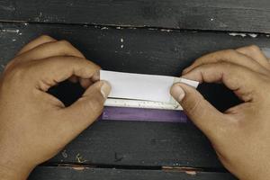 Man hand makes a cigarette with rolling traditional tools, hands closeup. photo