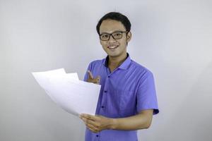 Young Asian Man is smile and happy when looking on paper document. Indonesian man wearing blue shirt. photo