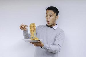 retrato de shock y wow joven asiático disfruta de fideos. comer el concepto de almuerzo. foto