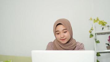 asian woman in hijab looking at her laptop screen at home photo