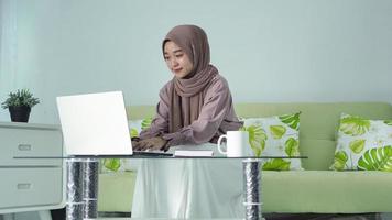 asian woman in hijab working from home using her laptop