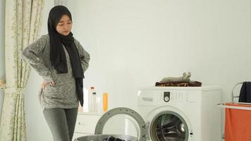 joven asiática mirando la cesta de ropa sucia en casa foto
