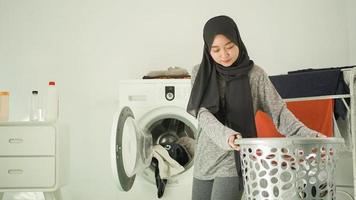 beautiful woman in hijab lifts clothes basket at home photo