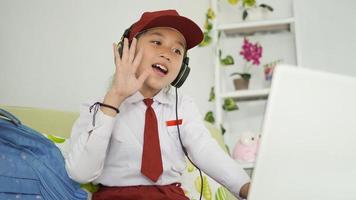 asian elementary school girl learning online greeting to laptop screen at home photo