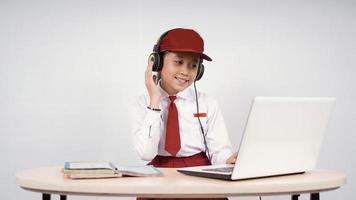 Niña asiática de la escuela primaria escuchando con auriculares mientras estudiaba aislada de fondo blanco foto