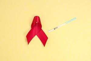 red ribbon and test pack symbol against HIV isolated on yellow background photo