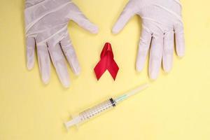 red ribbon with medical gloves and syringe against HIV isolated on yellow background photo