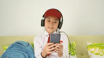 asian elementary school girl listening to something from smartphone at home photo