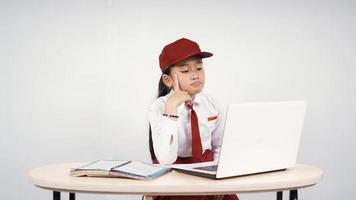 Elementary school asian girl looking for ideas on her laptop screen isolated on white background photo