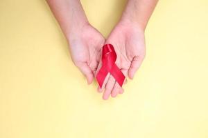 red ribbon in the palm of the hand against HIV isolated on yellow background photo