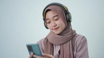 asian woman in hijab looking at phone screen while listening at home photo