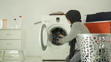 beautiful woman in hijab washing clothes in washing machine at home photo