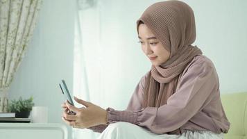 asian woman in hijab playing on her phone enjoying at home photo