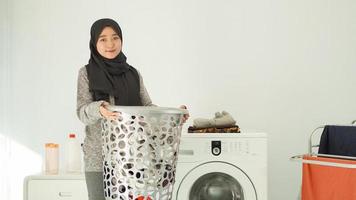 mujer asiática en hiyab trae una canasta de ropa para lavar en casa foto
