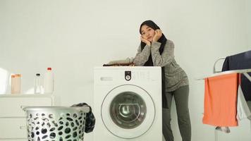 asian woman in hijab waiting for washing machine to spin at home photo