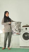 Asian woman in hijab standing carrying dirty clothes to wash at home photo