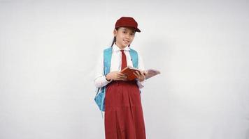 Niña de la escuela primaria asiática libro de apertura sonriendo aislado sobre fondo blanco. foto