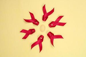 red ribbon and condom symbol against HIV isolated on yellow background photo