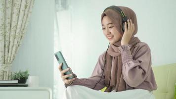 bella mujer con hiyab escuchando música divertida desde su smartphone en casa foto