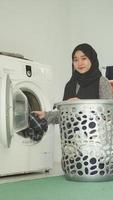 Asian woman in hijab puts dirty clothes in washing machine at home photo