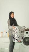 Asian woman in hijab brings a basket of clothes to wash at home photo