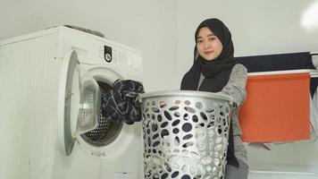 mujer asiática en hiyab pone ropa sucia en la lavadora en casa