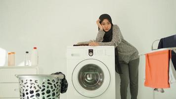 mujer asiática en hiyab esperando que la lavadora gire en casa foto