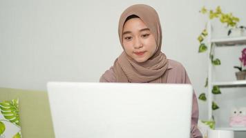 asian woman in hijab looking at her laptop screen at home photo