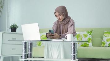 asian woman in hijab working from home looking for ideas from her smartphone photo