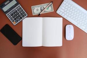 un cuaderno en blanco con bolígrafo se coloca en una mesa de oficina con herramientas informáticas y una variedad de materiales. antecedentes financieros y bancarios, endecha plana, vista superior foto