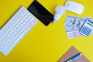 Blank notebook with a pen sits on an office desk table surrounded by computer tools and a range of materials. background in finance and banking, flat lay, top view photo